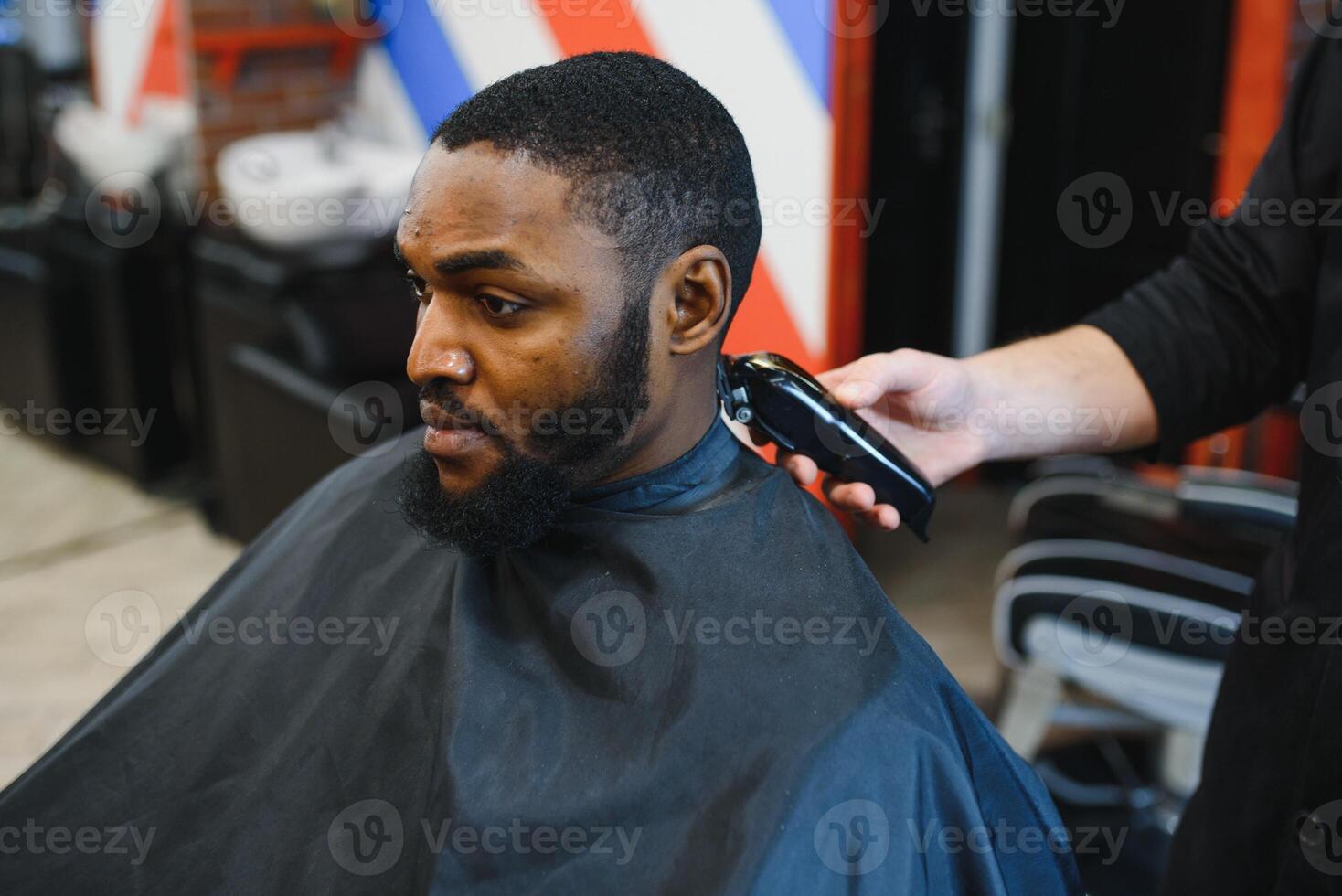 porträtt av ung svart man varelse trimmad med professionell elektrisk klippare maskin i barbershop.male skönhet behandling begrepp. ung afrikansk kille få ny frisyr i barberare salong foto