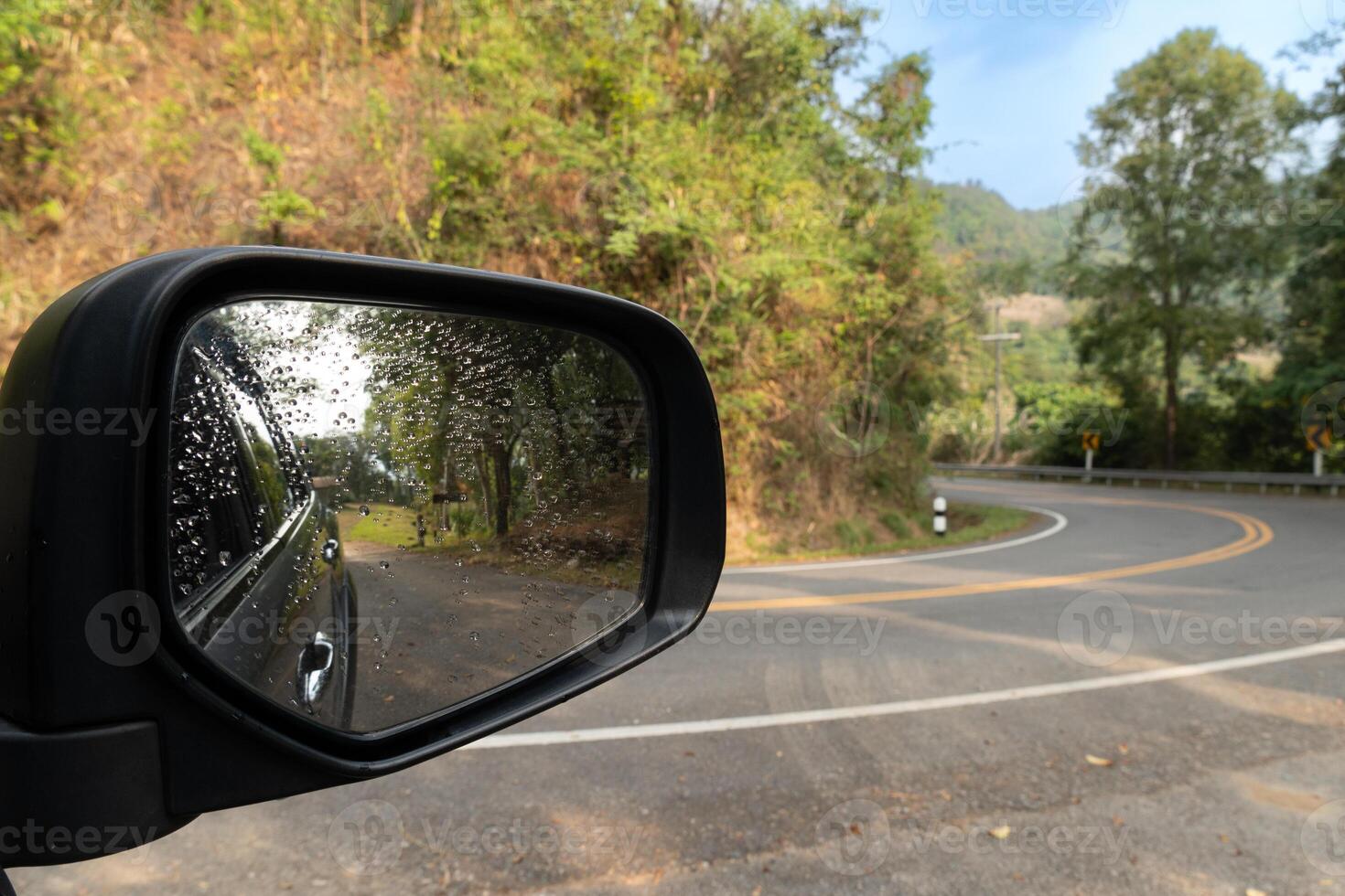 se av spegel bil kan se sida av bil se Bakom. böjd utför asfalt väg med bergen Nästa till den och vår lövverk. skog träd under de blå himmel. foto