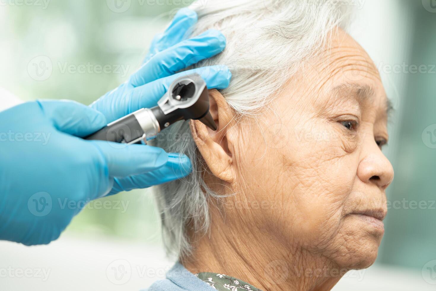 audiologist eller ent läkare använda sig av otoskop kontroll öra av asiatisk senior kvinna patient behandla hörsel förlust problem. foto