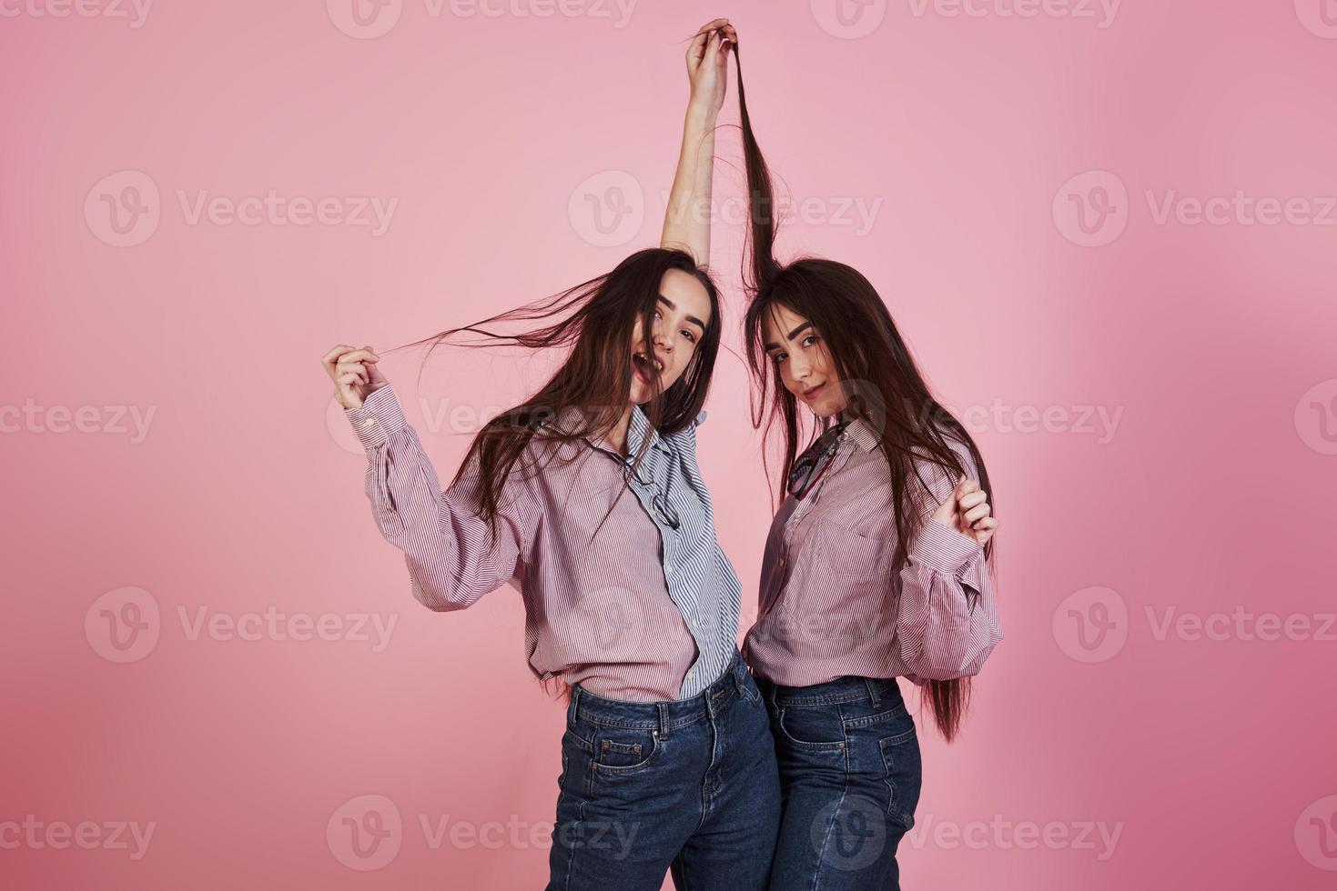 bara ludna lekfulla rörelser. unga kvinnor som har kul i studion med rosa bakgrund. bedårande tvillingar foto