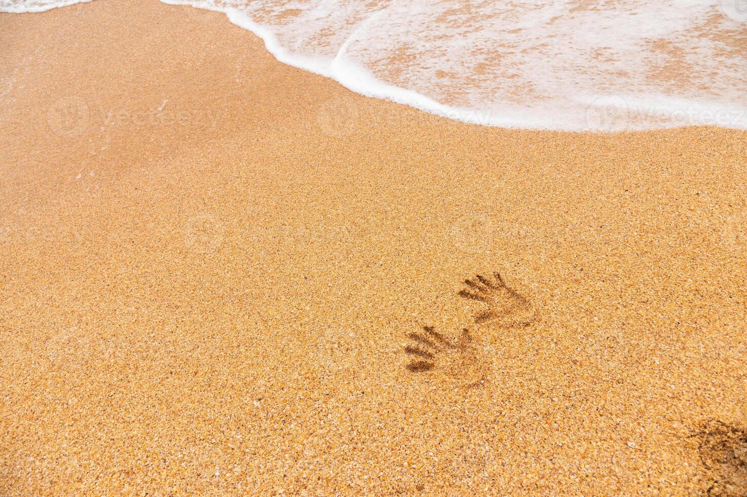 mänsklig spår av två hand grafik på en sandig strand utan människor, hav vågor rullande i från de sida foto