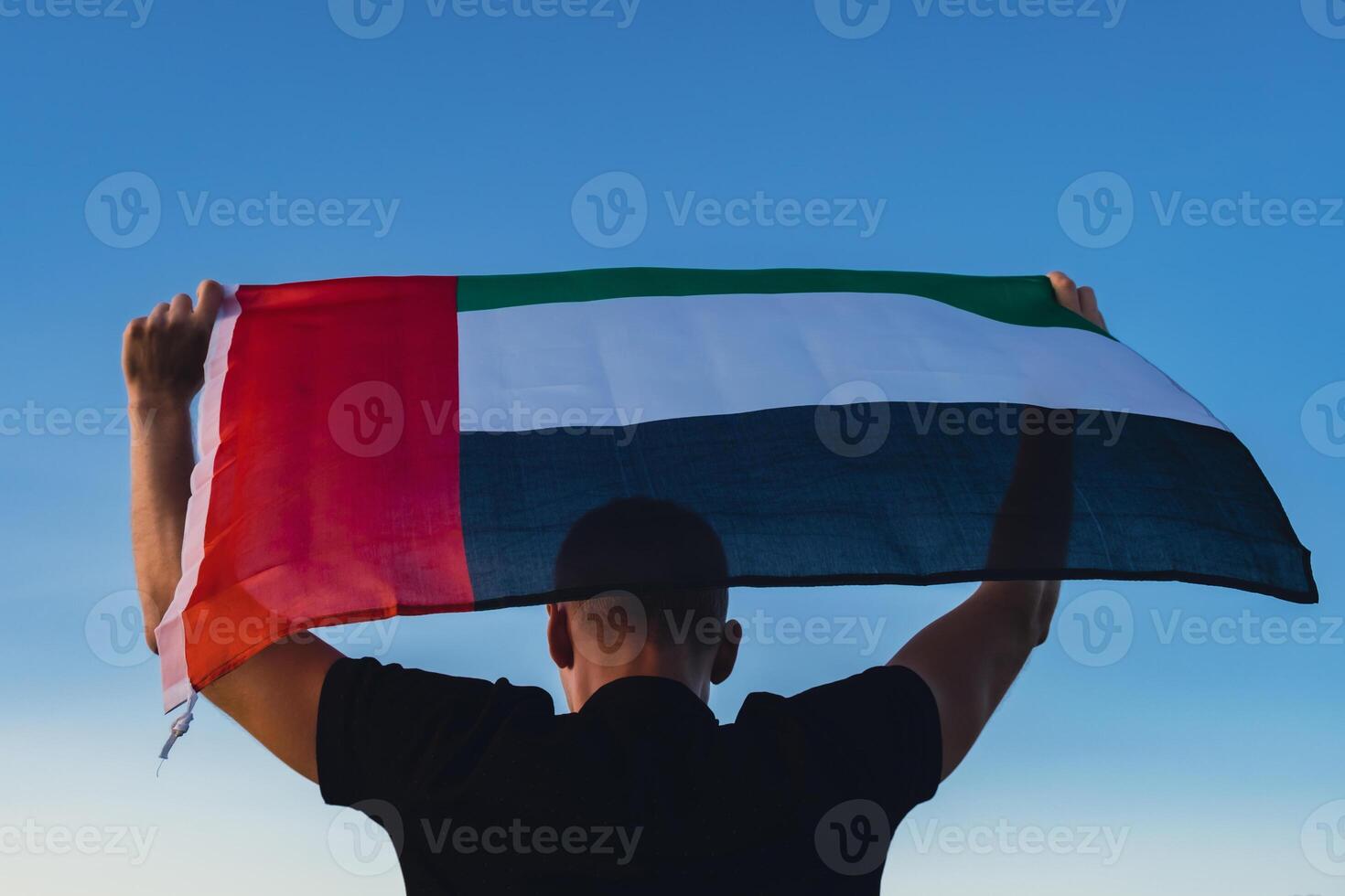 man innehav nationell flagga av uae vinka i de vind solnedgång. flagga av förenad arab emirates på Sol bakgrund. tecken av dubai. anda av de union nationell oberoende dag eller flagga dag foto