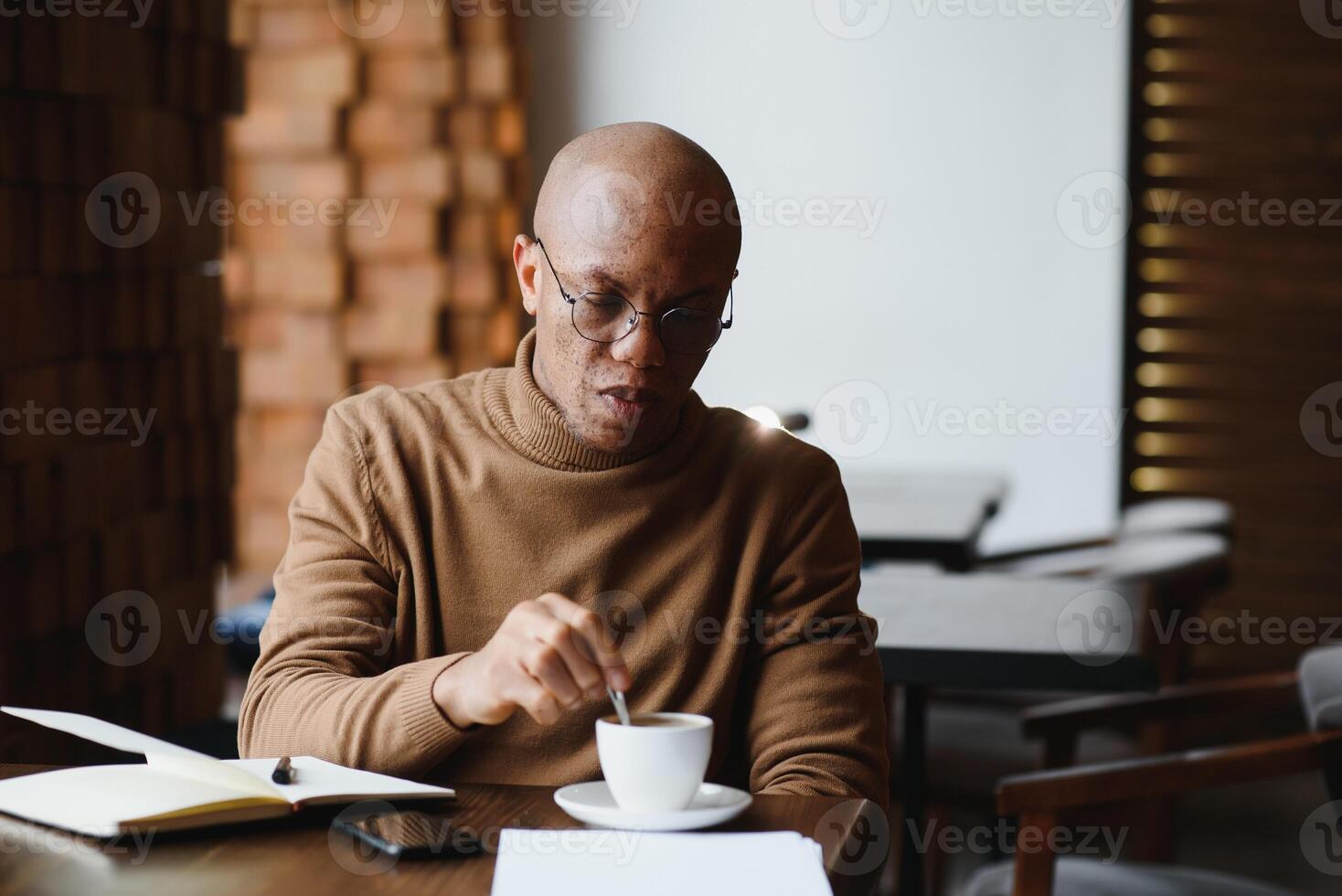 koncentrerad svart manlig entreprenör läser papper dokument Sammanträde i Kafé med kaffe nära fönster foto