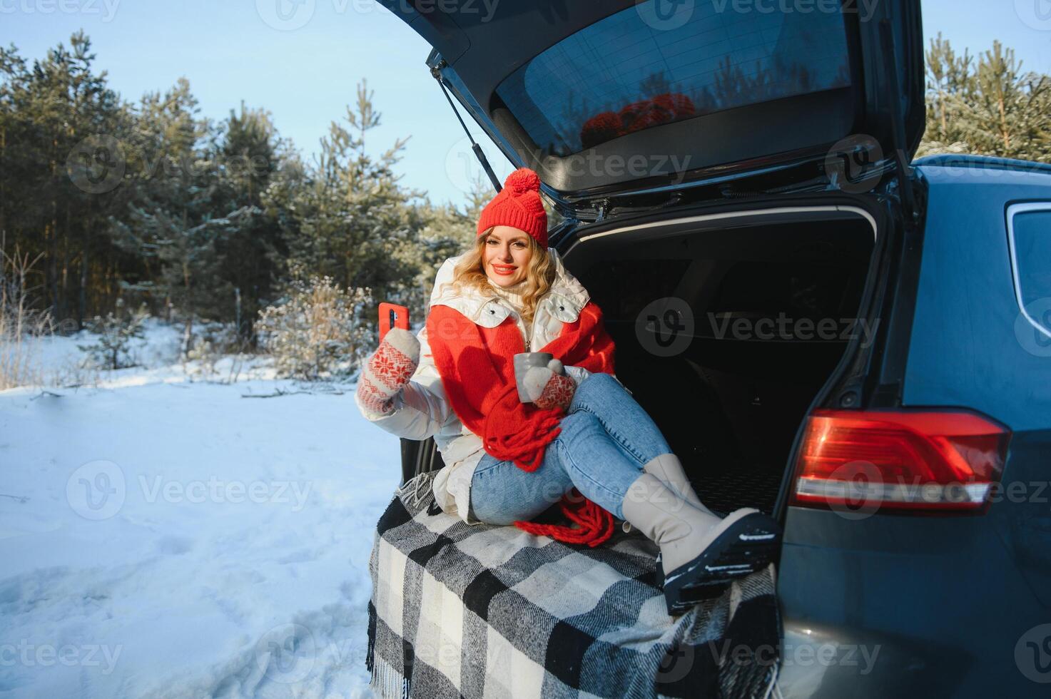 ung kvinna Sammanträde i bil trunk dricka värma te och tar en selfie på vinter- snöade dag. foto