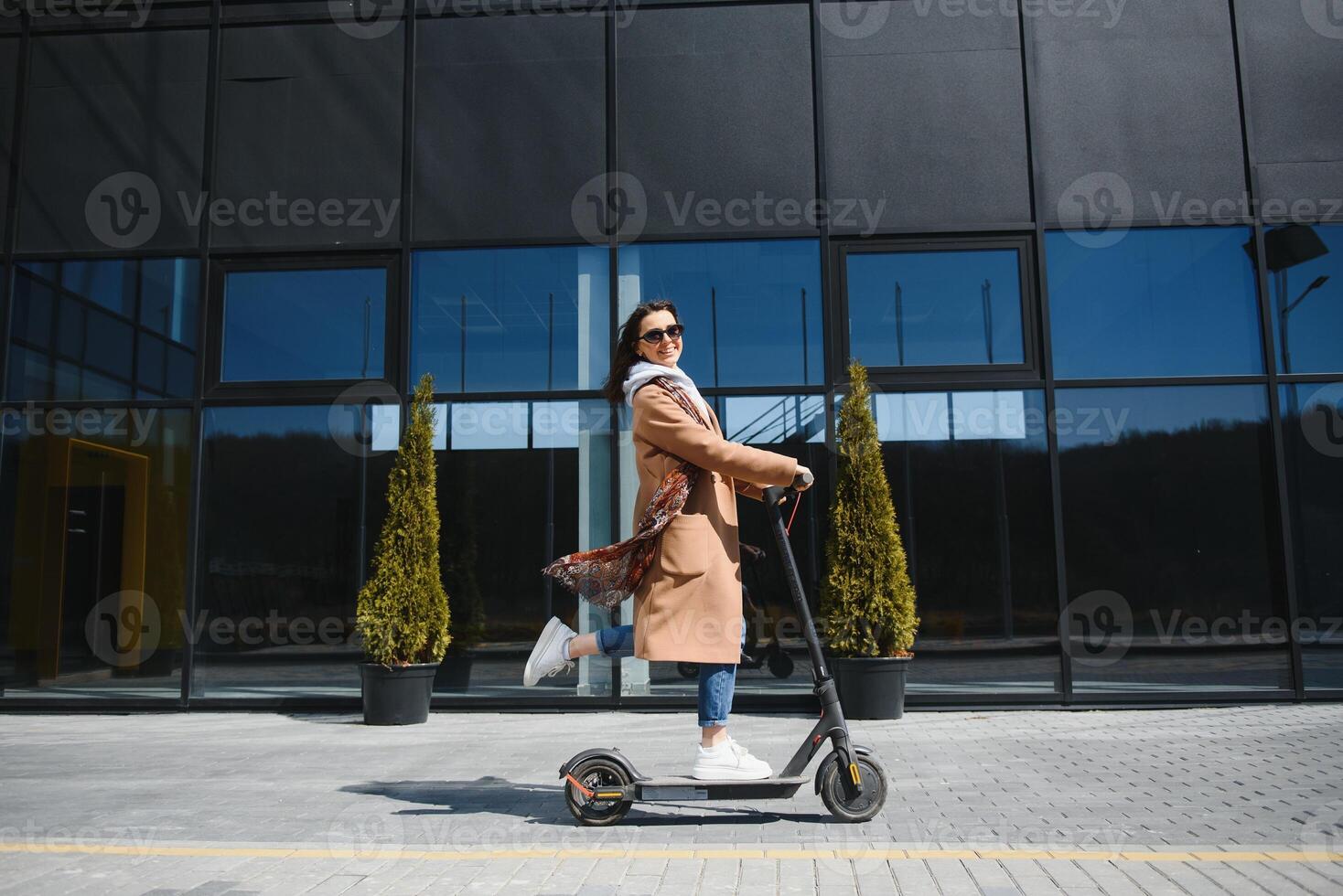 ung kvinna på de elektrisk skoter på de bakgrund av kontor byggnad, skoter foto