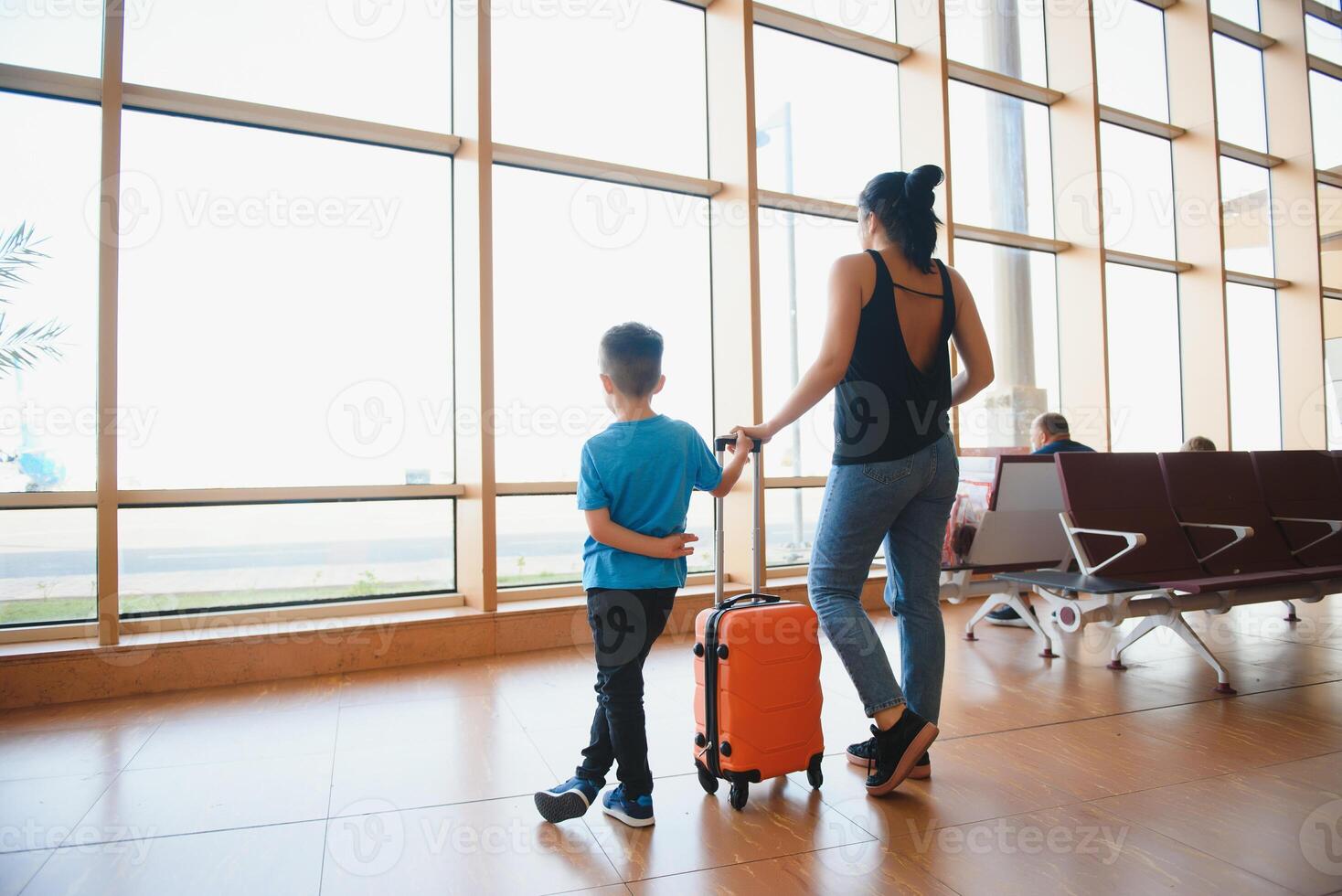 familj på flygplats innan flyg. mor och son väntar till styrelse på avresa Port av modern internationell terminal. reser och flygande med barn. mamma med bebis och litet barn ombordstigning flygplan. foto