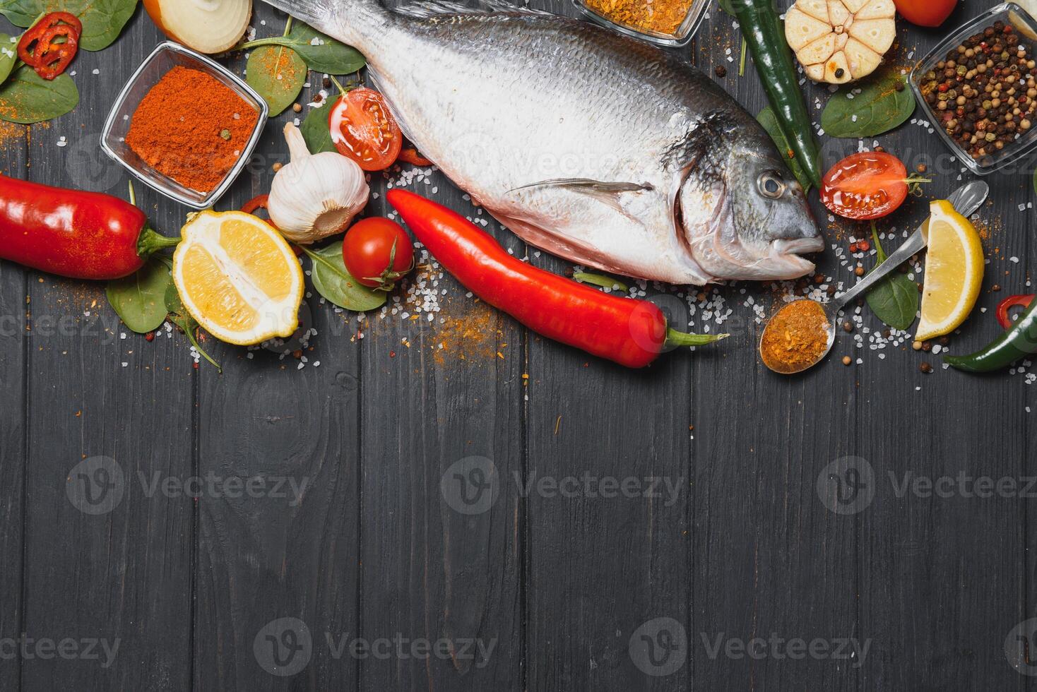 rå hav fisk dorado med citron, peppar, tomater och olika kryddor. på en svart rustik bakgrund. foto