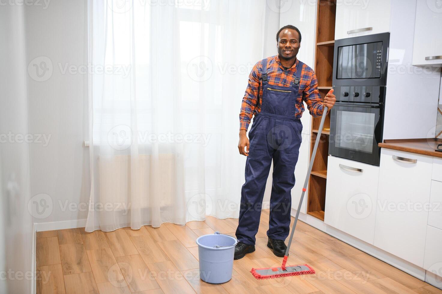 ung afrikansk man tvättar de golv med en mopp i de rum foto