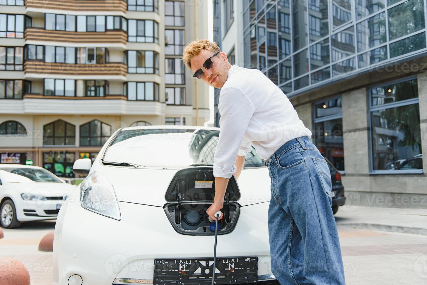 en stilig ung man är laddning hans modern elektrisk bil. foto