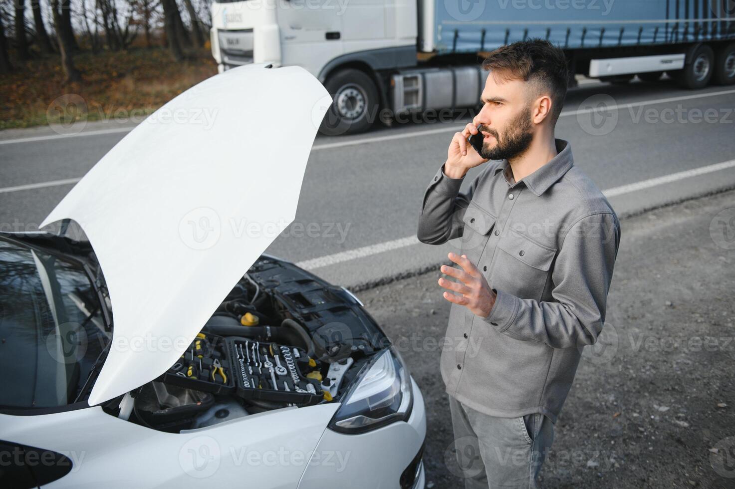 man använda sig av en mobiltelefon ring upp garage i främre av de öppen huva av en bruten bil på de väg i de skog. bil bryta ner begrepp. foto