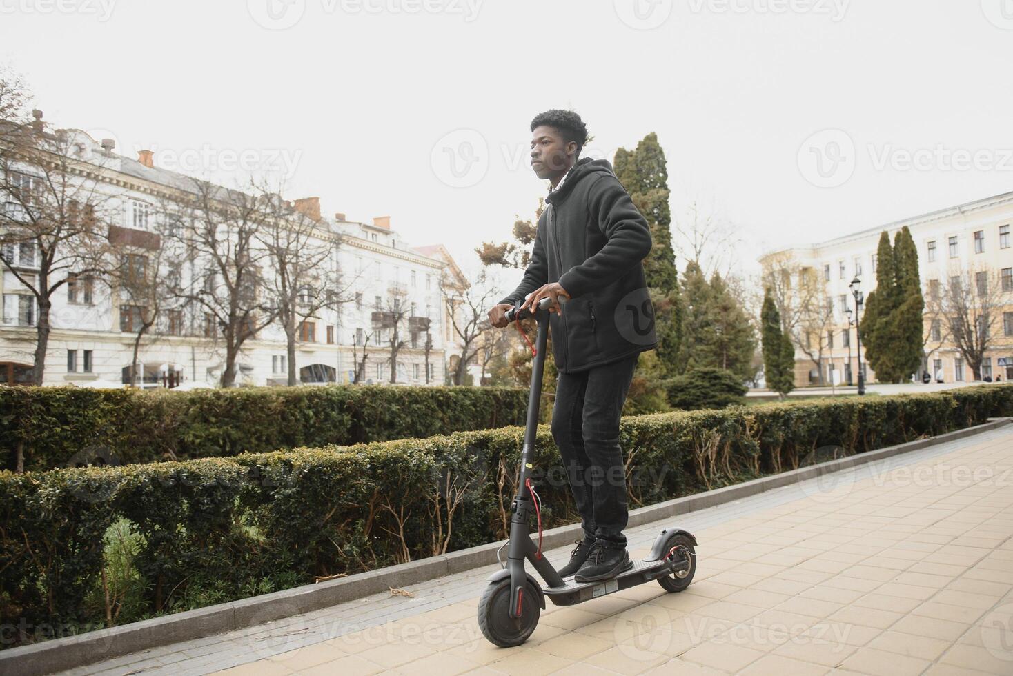 afro amerikan kille rider ett elektrisk skoter mot de bakgrund av en vägg, en studerande användningar eco transport foto