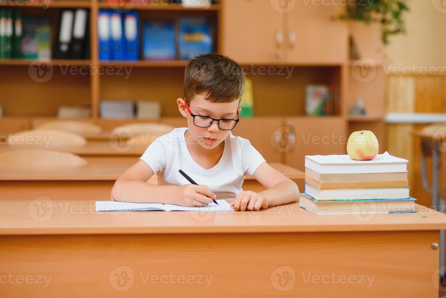 elementärt skola pojke på klassrum skrivbord påfrestande till hitta ny idéer för skolarbete. foto