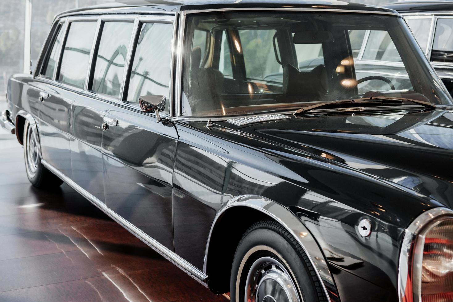 fram- och sidovy av svart retro limousine i businessklass med höger strålkastare, kromspegel och hjulhus på brunt golv foto