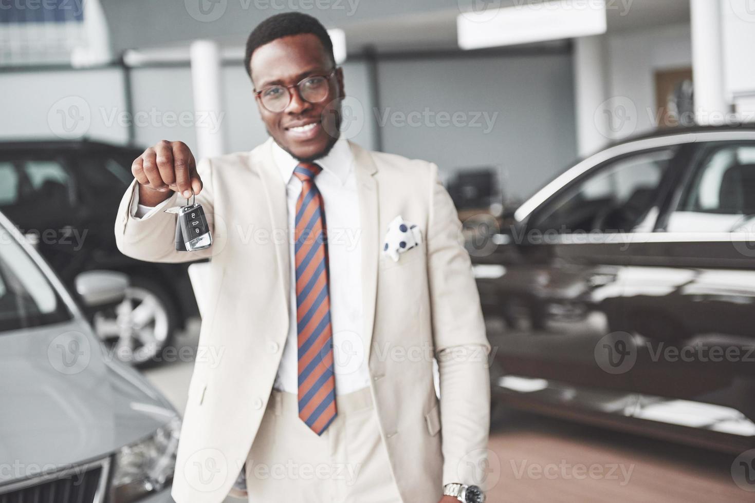 den unga attraktiva svarta affärsmannen köper en ny bil, han håller nycklarna i handen. drömmar går i uppfyllelse foto