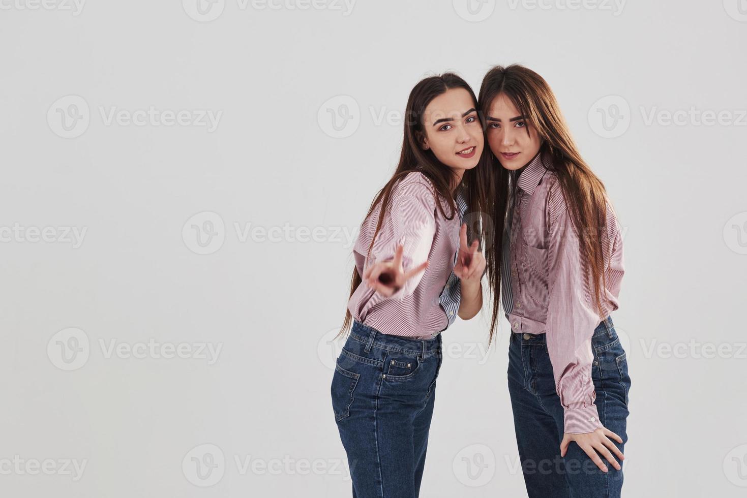 tittar rakt in i kameran och visar gester. två systrar tvillingar står och poserar i studion med vit bakgrund foto