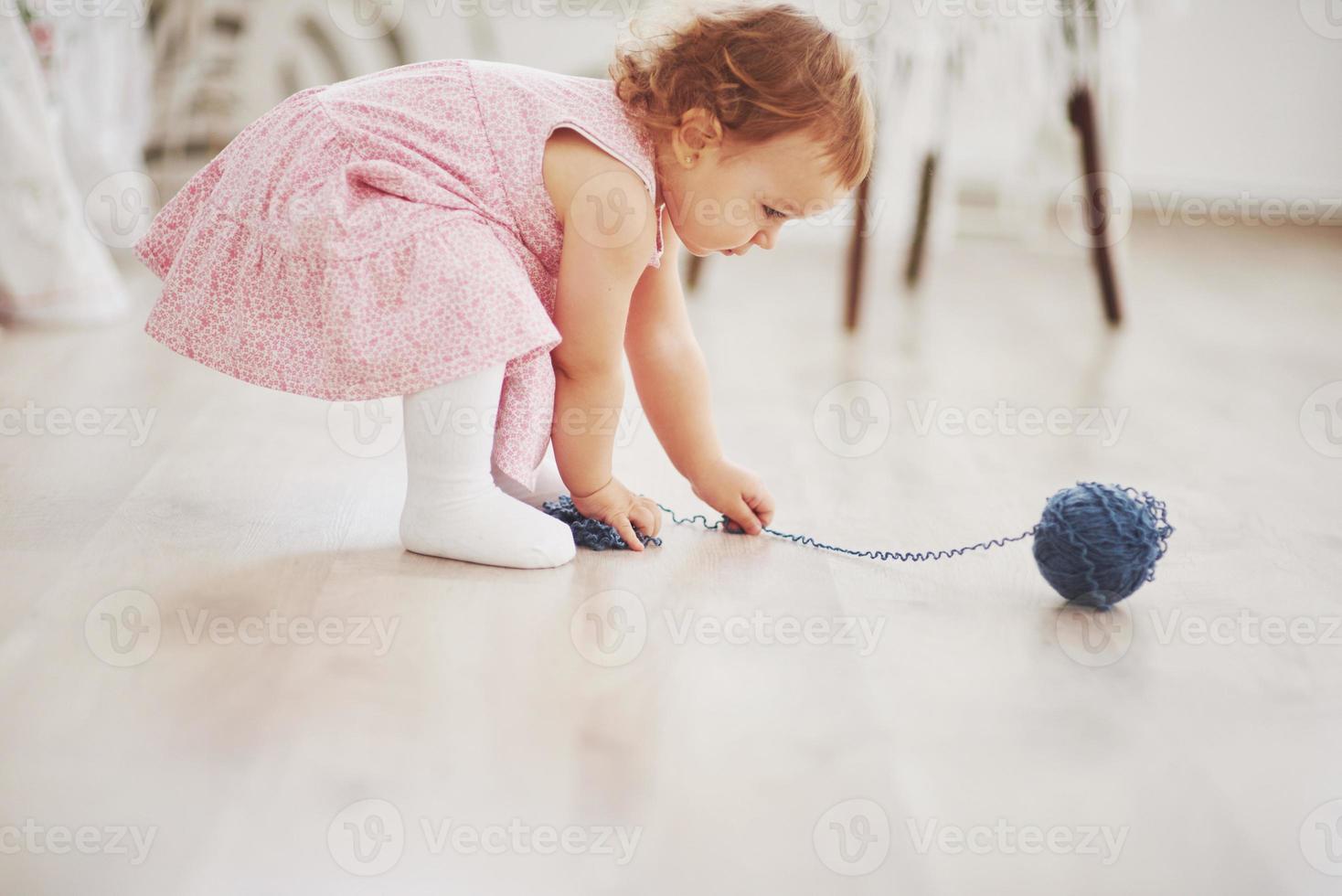 barndomskoncept. flicka i söt klänning leker med färgad tråd. vitt vintage barnrum foto