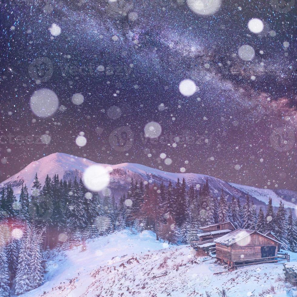 natt i de stora Karpaterna. Vintergatan på himlen och hus gjorda av trä på kullen foto