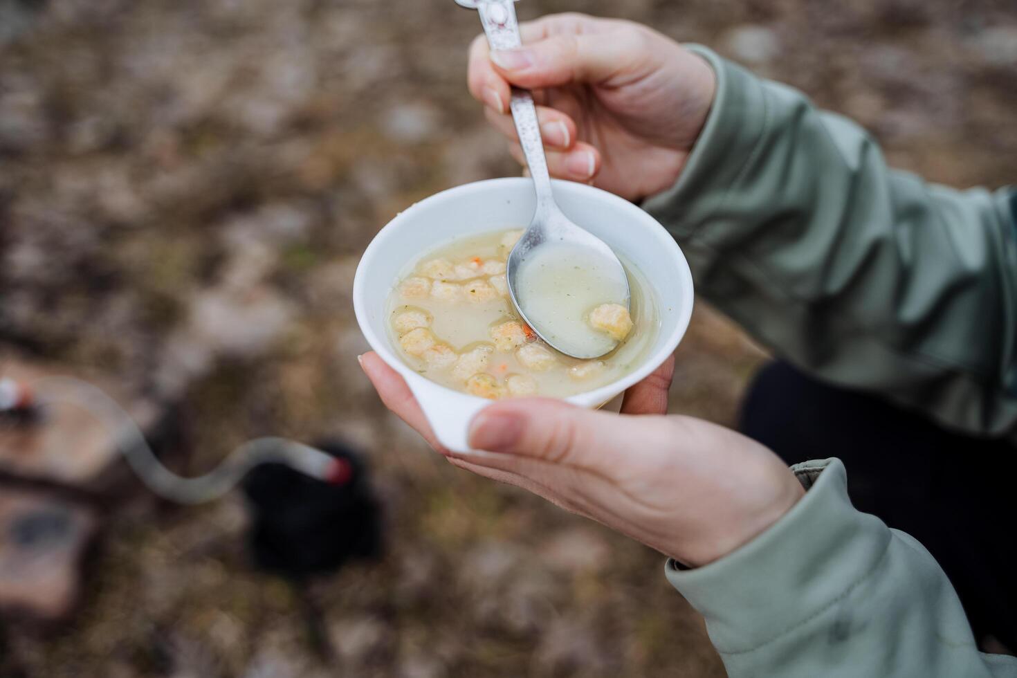 ärta soppa med ströbröd i en tallrik, håll en kopp med mat med din händer, äta mat med en sked på en vandra, en turisternas lunch är filmad närbild, en snabbt måltid, en ljus frukost. foto
