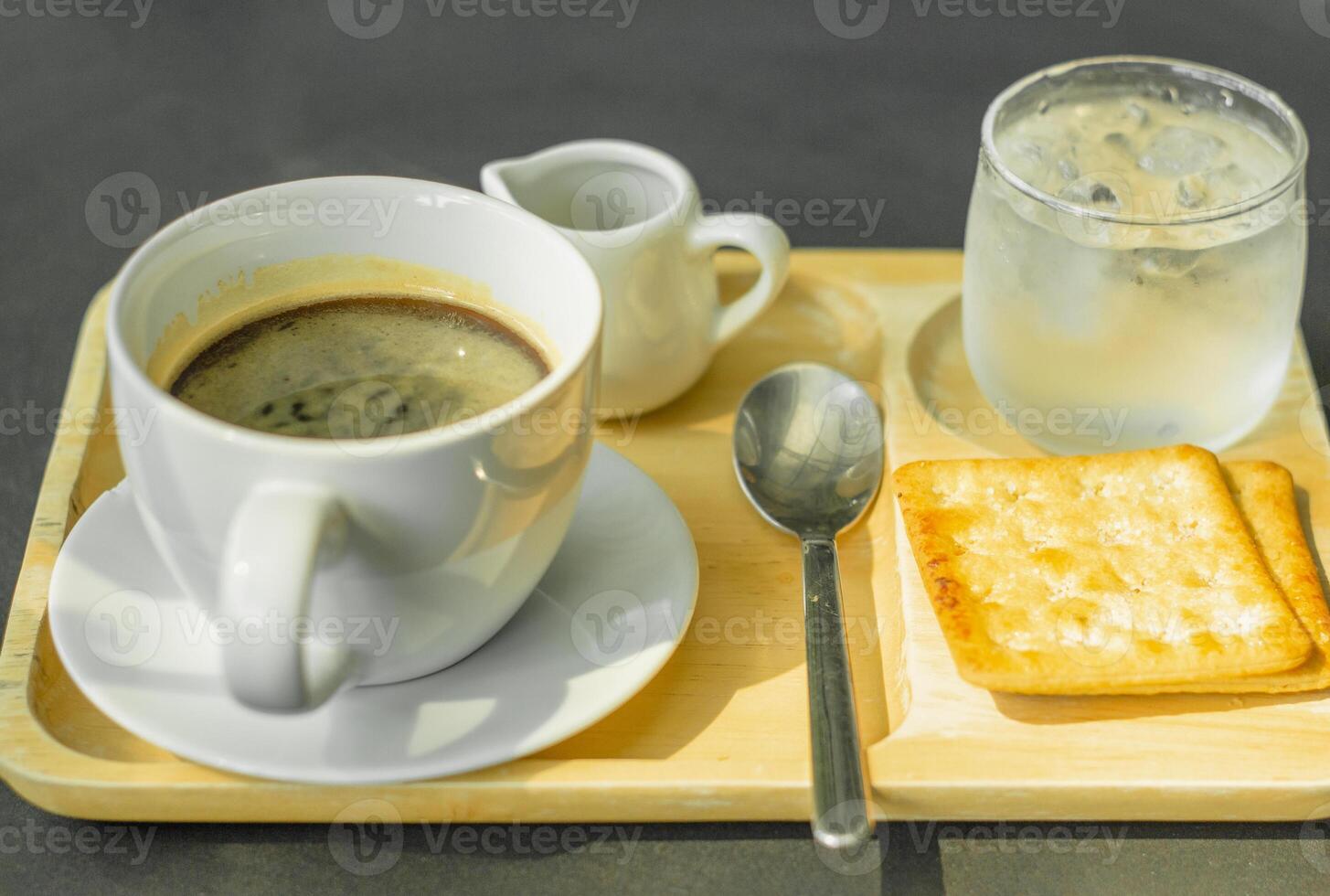 varm americano kaffe på en trä- bricka med crackers och kall vatten. foto