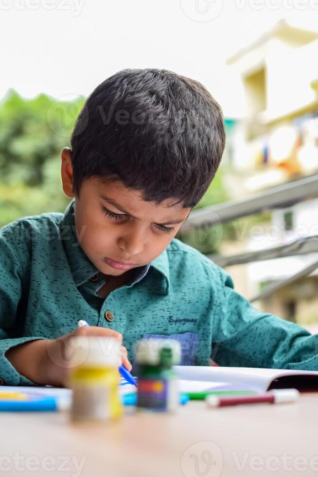 smart indisk liten pojke prestera tumme målning med annorlunda färgrik vatten Färg utrustning under de sommar semester, söt indisk unge håller på med färgrik tumme målning teckning på trä- tabell foto