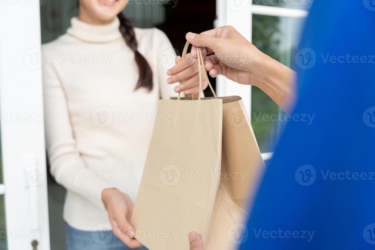 leende asiatisk kvinna mottar papper väska paket av mat från kurir främre hus. leverans man skicka leverera uttrycka. uppkopplad handla, papper behållare, hämtmat, brevbärare, leverans service, paket foto