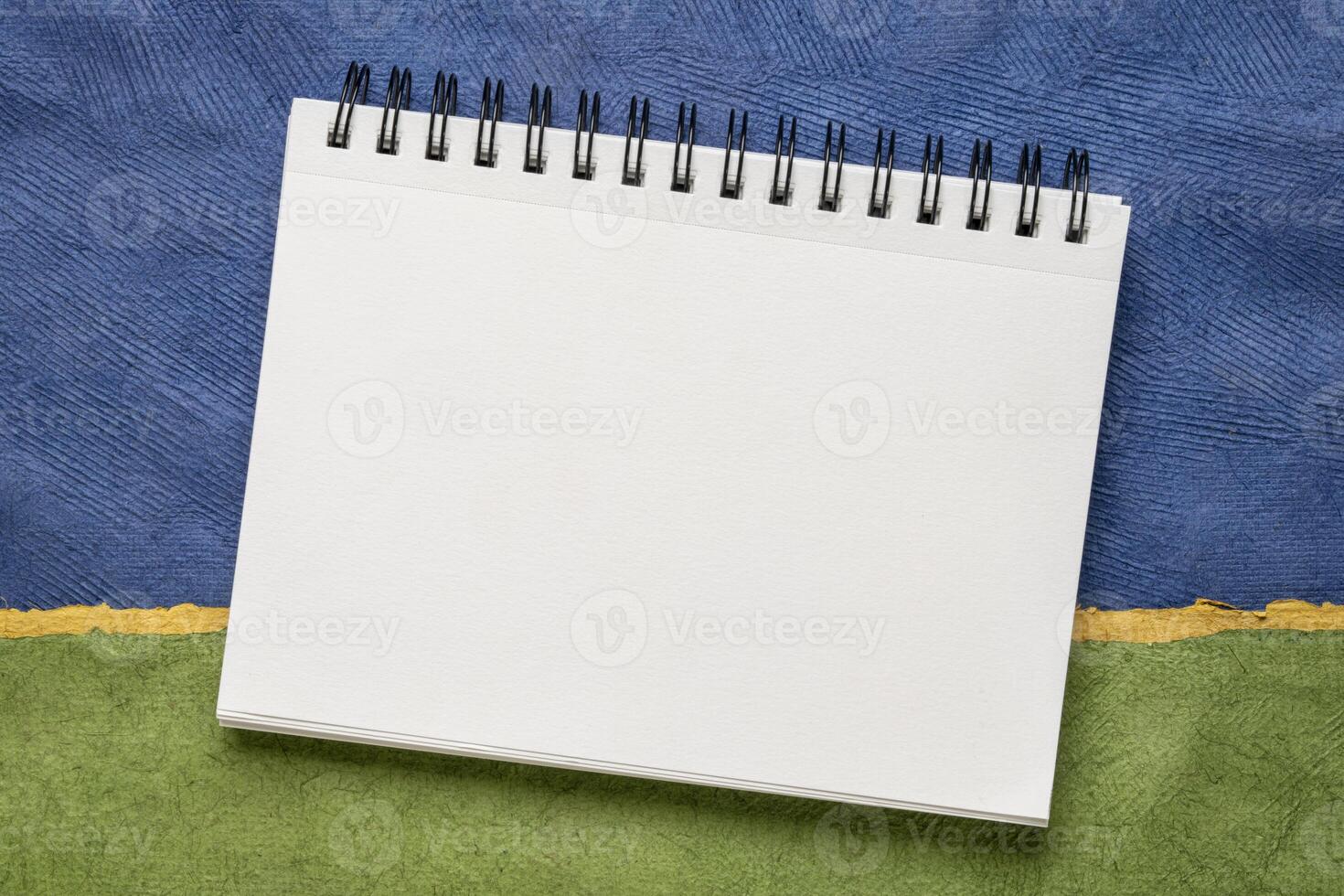 tom spiral skissbok med vit sidor mot färgrik abstrakt papper landskap foto