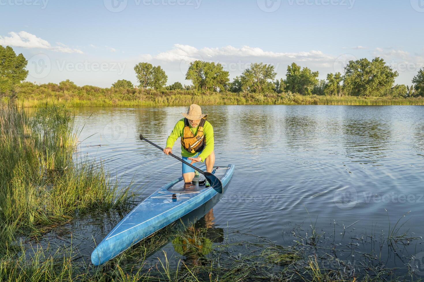 senior manlig stå upp paddlare är landning på en gräs- sjö Strand, sommar landskap i colorado foto