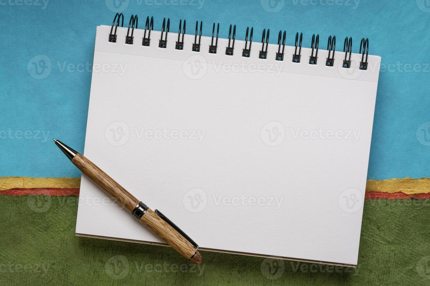 tom spiral skissbok med vit sidor med en penna mot färgrik abstrakt landskap foto