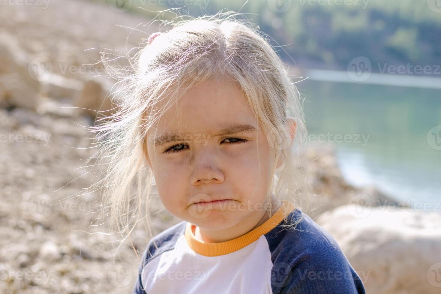 liten flicka med blond hår ser på de kamera med en ledsen uttryck på henne ansikte foto