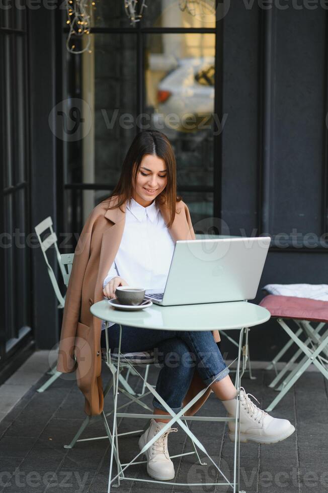 Lycklig trevlig kvinna arbetssätt på bärbar dator i gata Kafé foto