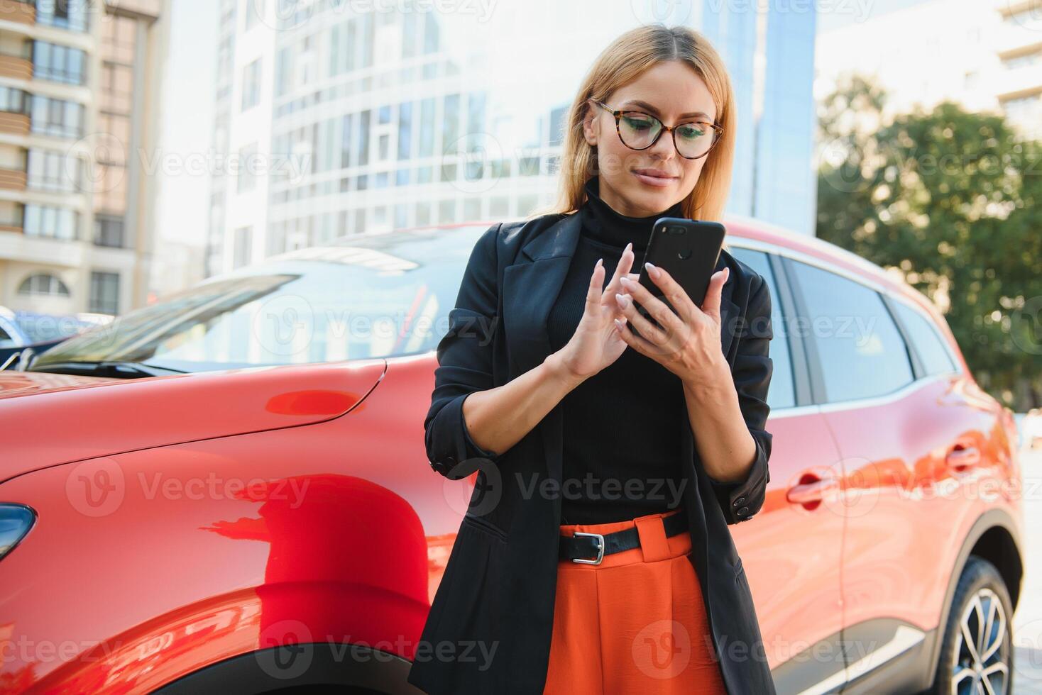 kvinna använder sig av mobil telefon, kommunikation eller uppkopplad Ansökan, stående nära bil på stad gata eller parkering, utomhus. bil delning, uthyrning service eller taxi app. foto