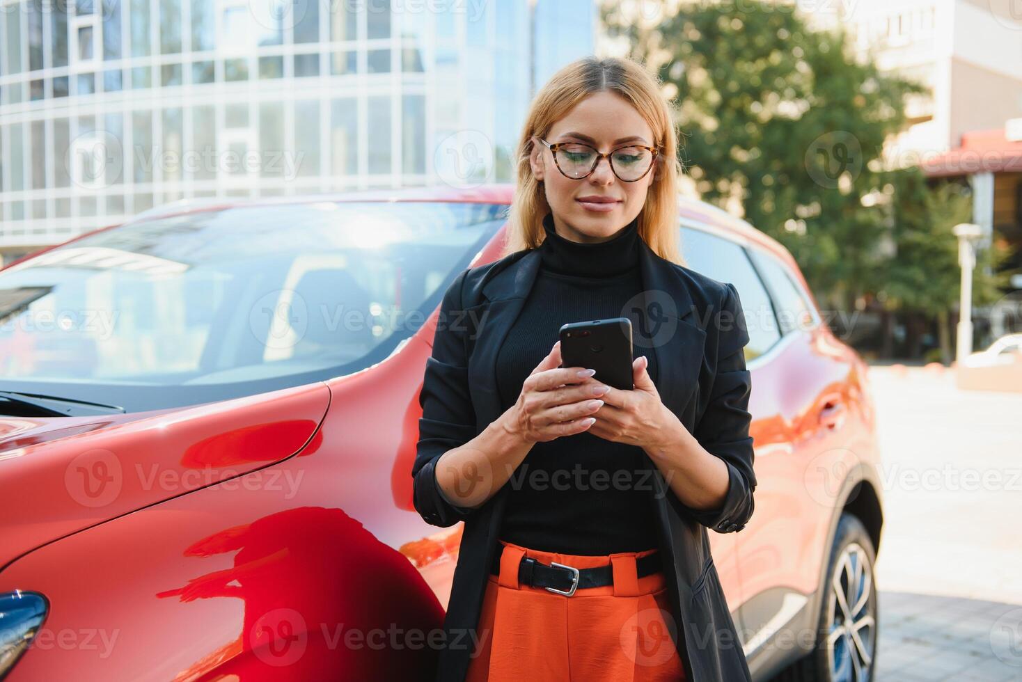 kvinna använder sig av mobil telefon, kommunikation eller uppkopplad Ansökan, stående nära bil på stad gata eller parkering, utomhus. bil delning, uthyrning service eller taxi app. foto