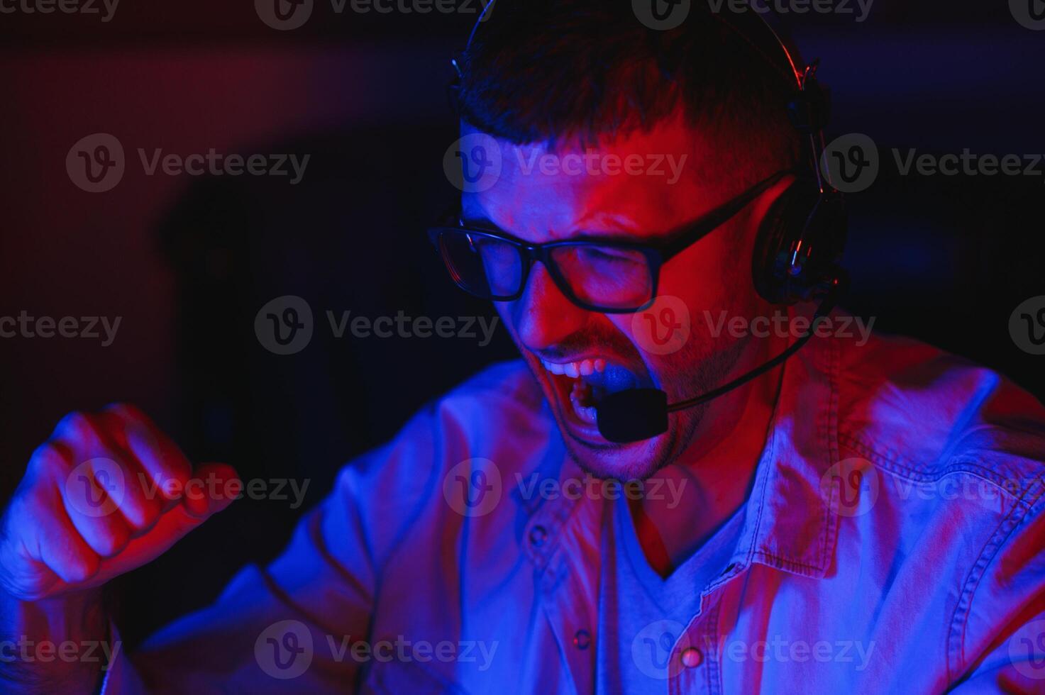 professionell gamer spelar video spel på hans dator. han är deltar i uppkopplad cyber spel turnering eller i internet Kafé. han bär glasögon och samtal in i mikrofon. foto