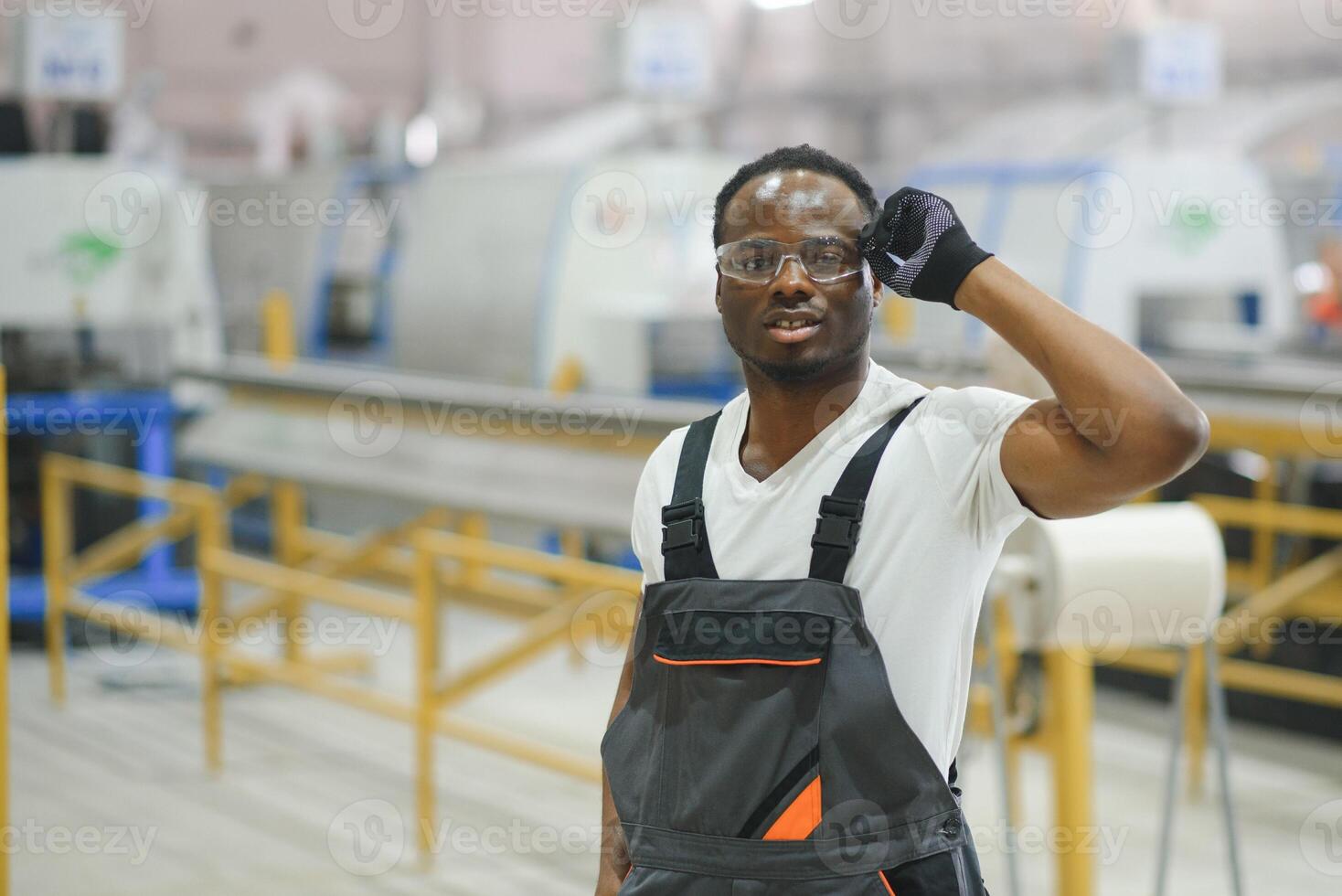 porträtt av afrikansk amerikan manlig ingenjör i enhetlig och stående i industriell fabrik foto