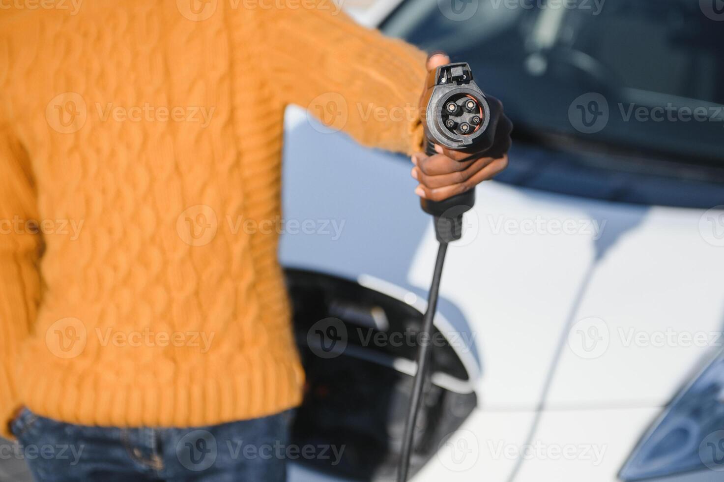 stänga upp av manlig hand innehav elektrisk laddning plugg för lyx röd bil. afrikansk affärsman laddning hans bil på station. eco vänlig transport. foto