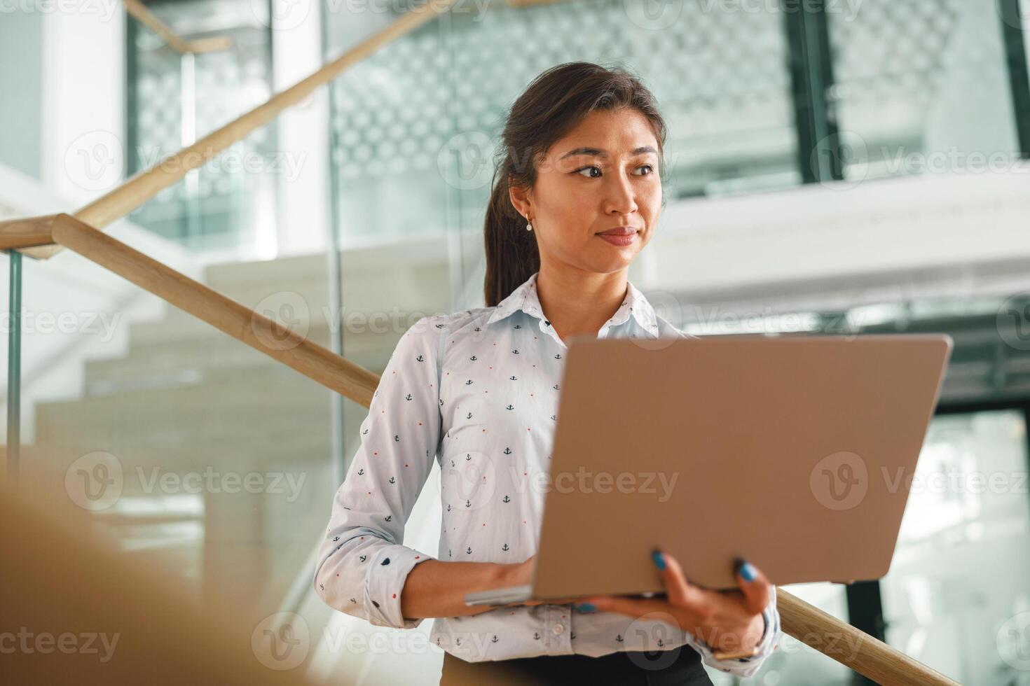 fokuserade kvinna chef stående med bärbar dator och ser på sida på kontor bakgrund foto
