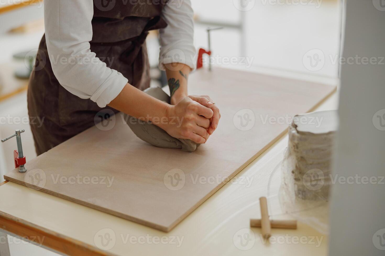 stänga upp av kvinna krukmakare i förkläde knådar bit av lera med henne händer på tabell i studio foto