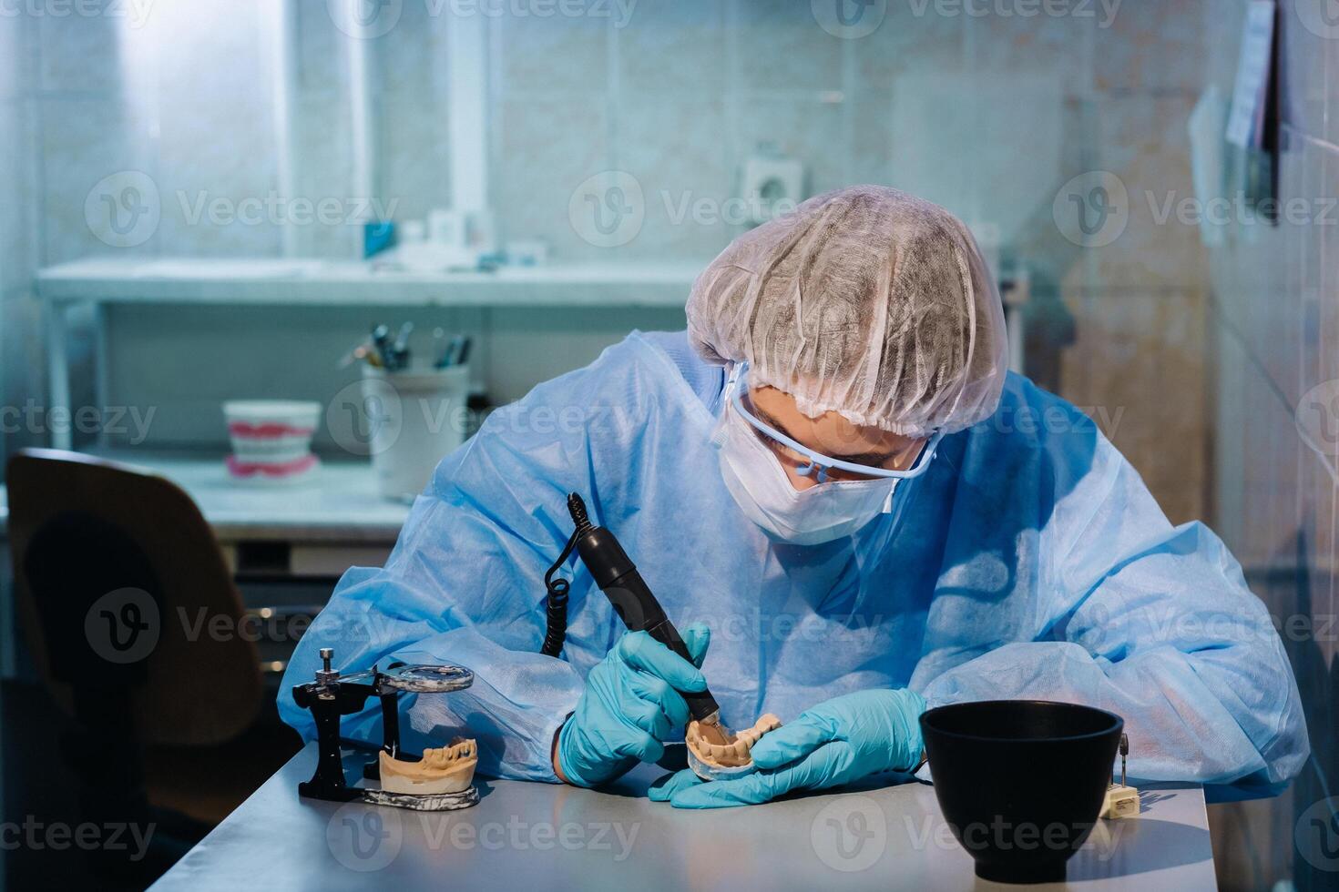 en dental tekniker i skyddande Kläder är arbetssätt på en protes- tand i hans laboratorium foto