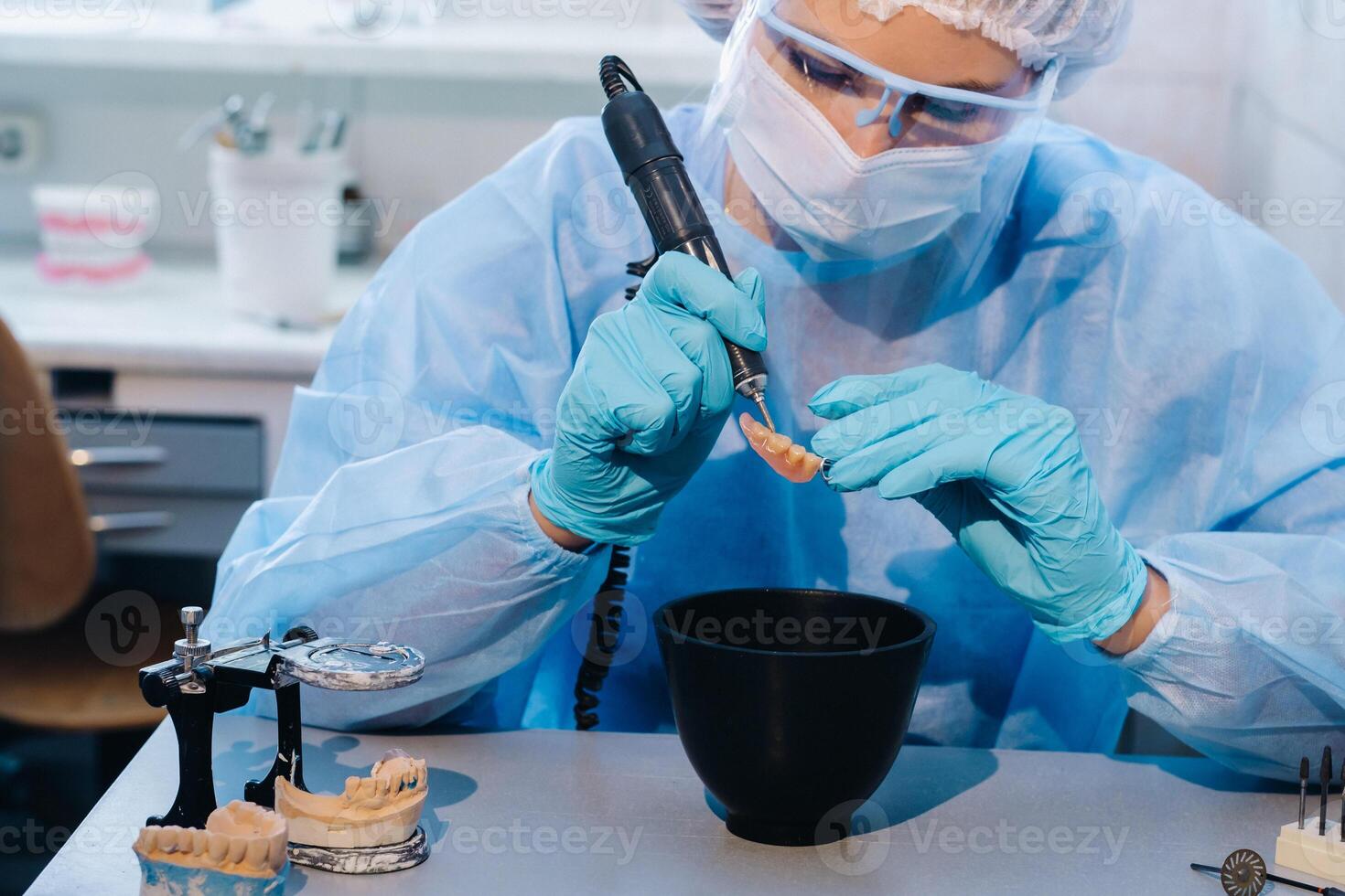 en dental tekniker i skyddande Kläder är arbetssätt på en protes- tand i hans laboratorium foto