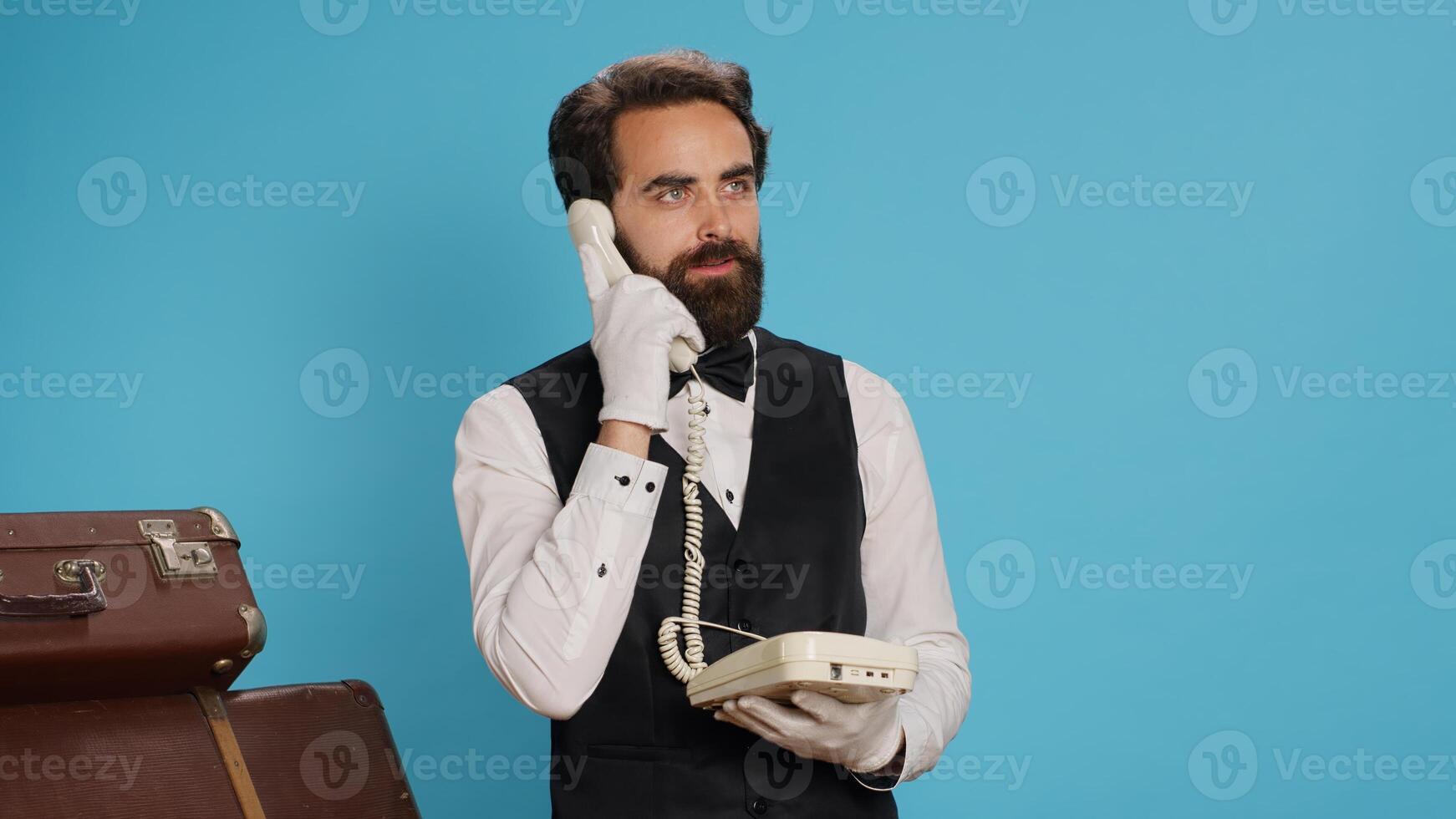 lyxig piccolo svar fast telefon telefon ring upp i studio, talande till resenärer handla om rum boende. elegant professionell hotell porter använder sig av telefon med sladd till ta samtal, årgång grej. foto