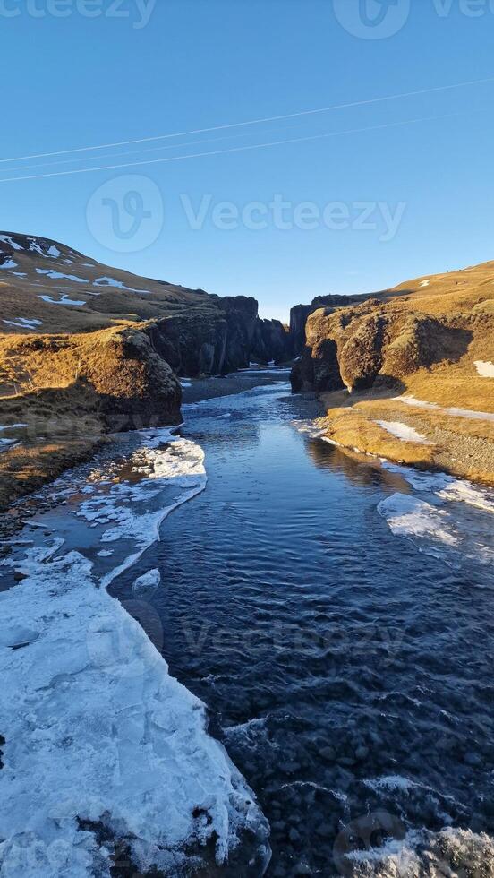 snöig isländsk kanjon med frysta vatten ström och klippor täckt i frost skapande underbar landskap se. magisk fjadrargljufur kanjon med flod strömma i island mellan backar. foto