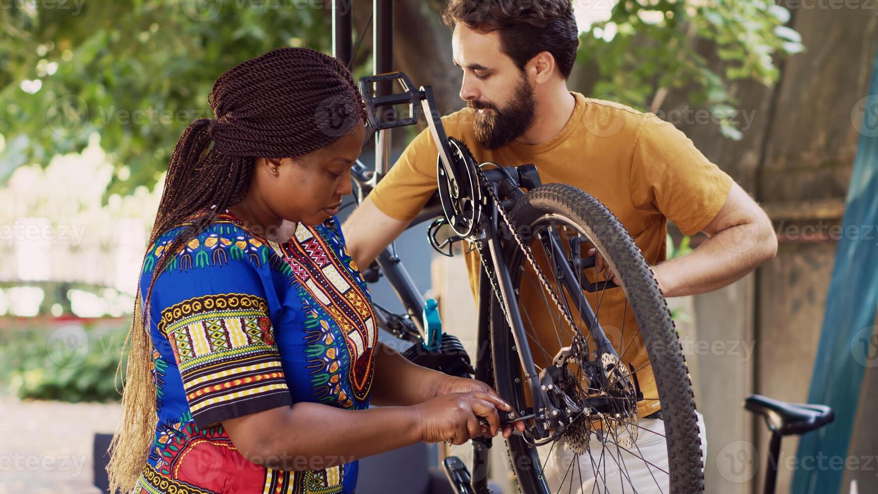 multietnisk par arbetssätt tillsammans till reparera och upprätthålla skadad cykel för sommar cykling. caucasian pojkvän hjälper flickvän i välja lämplig verktyg för fixering cykel nav och axel i gård. foto