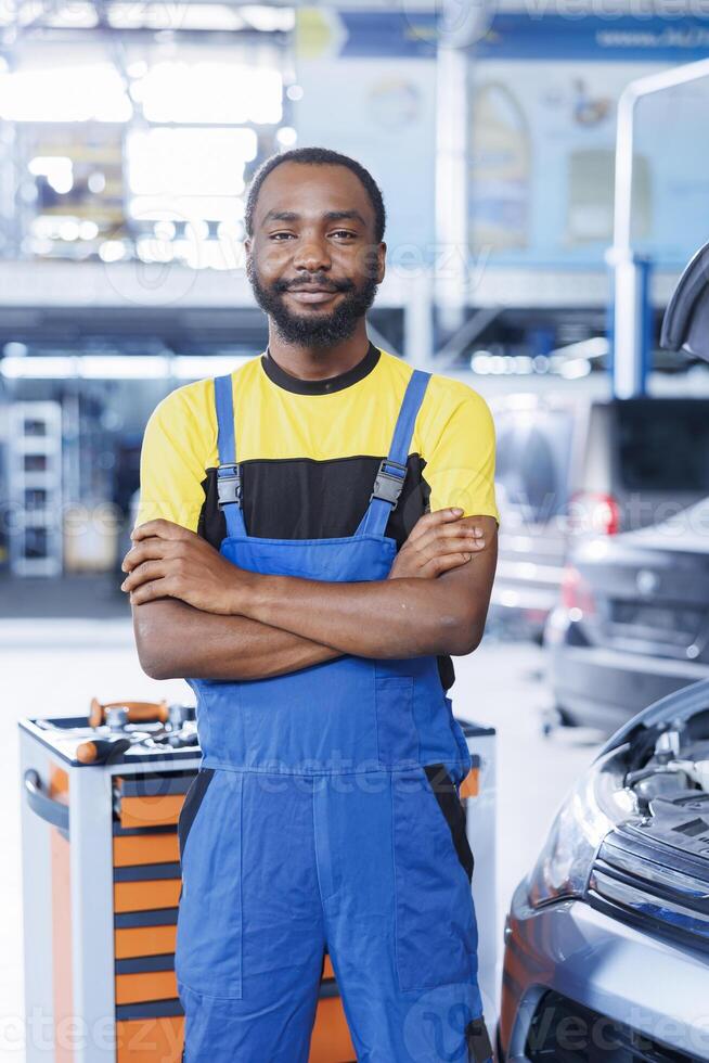 porträtt av stolt bipoc serviceman i bil reparera affär uppdrag med ändring bilar olja. licensierad specialist i garage redo till Start håller på med kontroller på fordon i garage arbetsyta foto