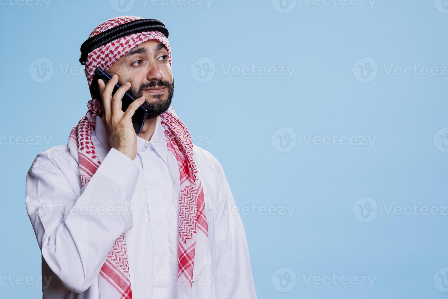 muslim man klädd i islamic kläder, svar ring upp och har konversation på mobil telefon. arab person klädd i traditionell thobe och ghutra medan talande på smartphone foto