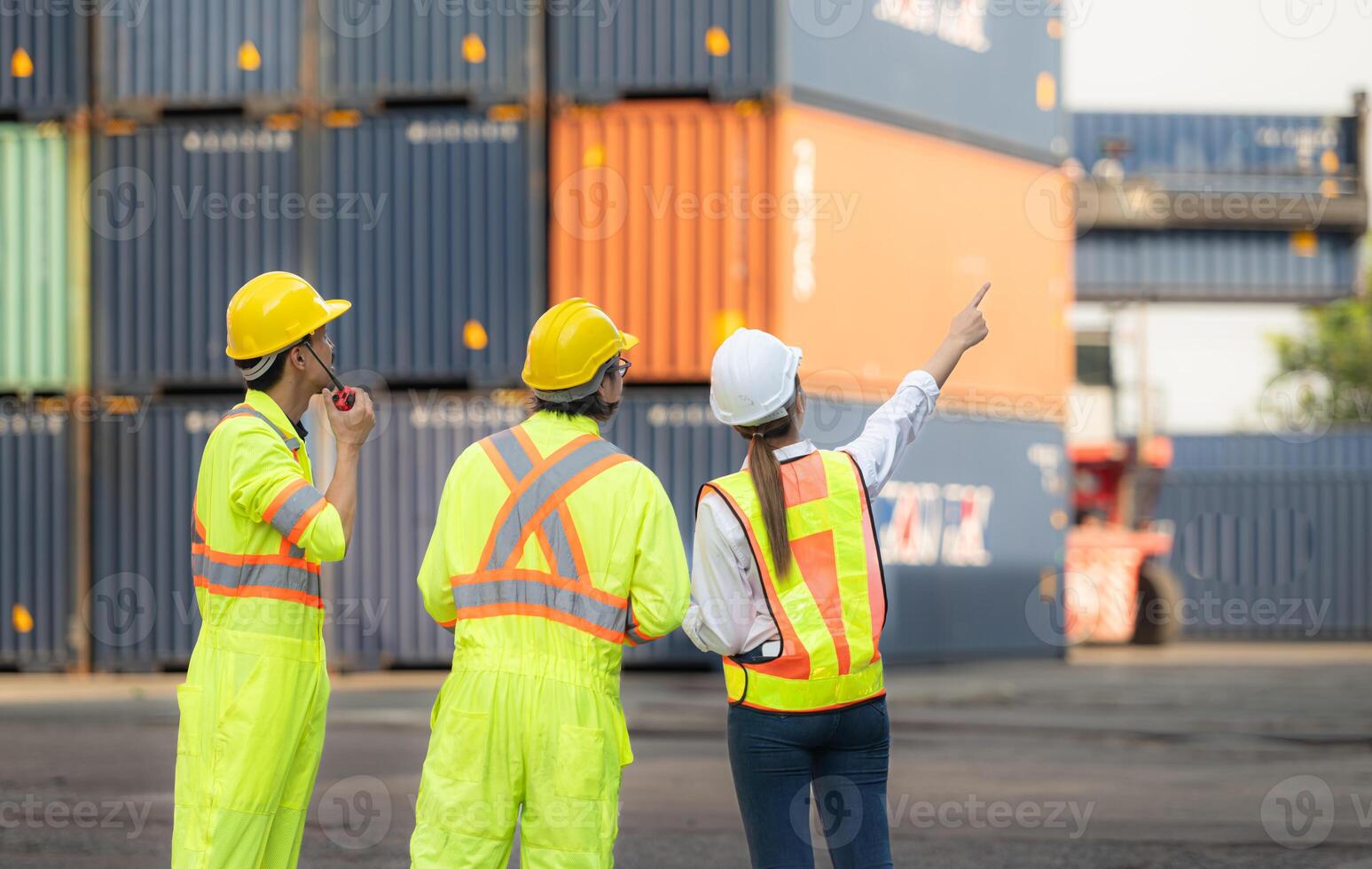 grupp av arbetare i de importera och exportera industri använda sig av walkie talkies till kommunicera med drivrutiner av nå stacker behållare i ett tömma behållare lager. foto