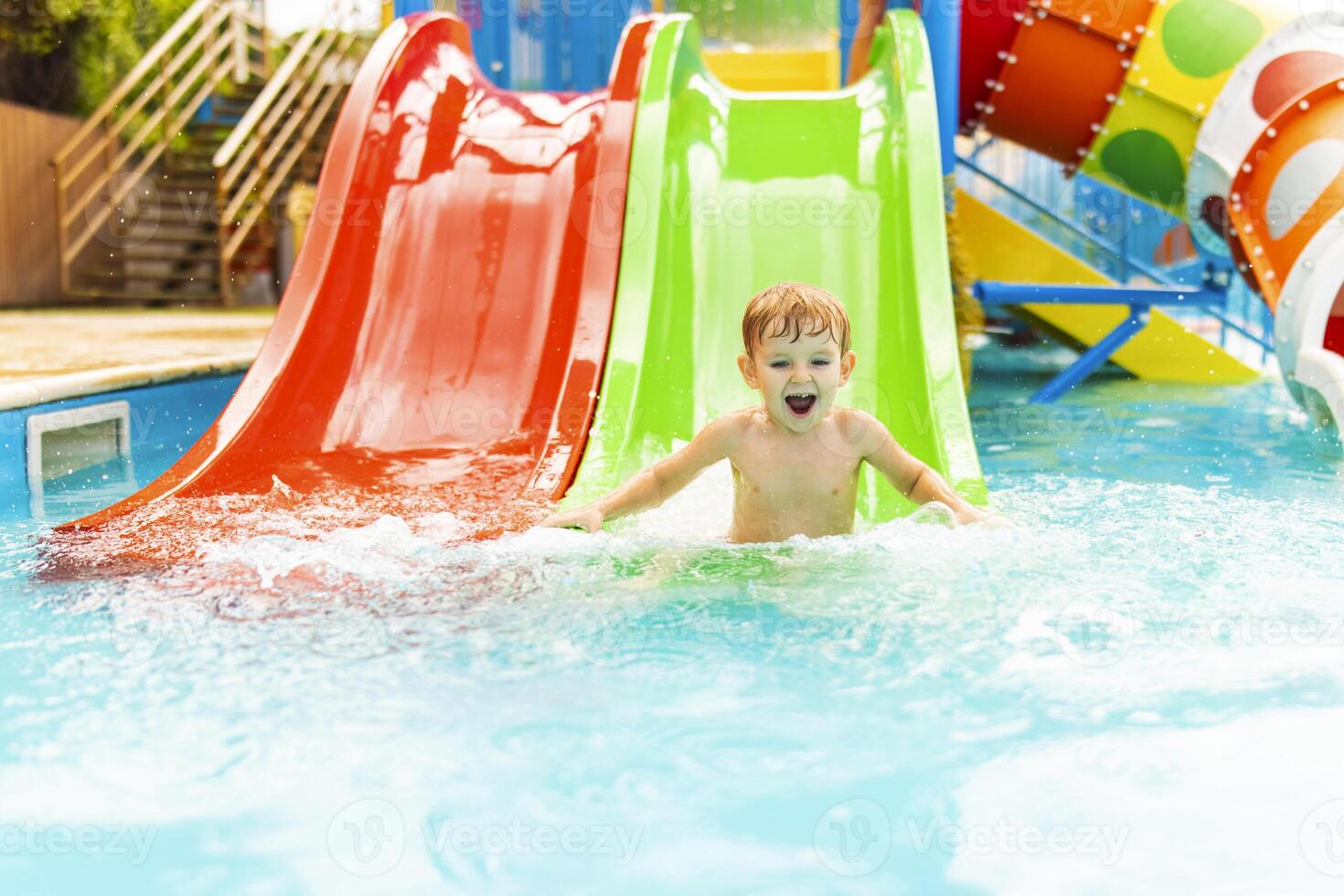 liten pojke spelar på vatten glida i utomhus- slå samman på en varm sommar dag foto