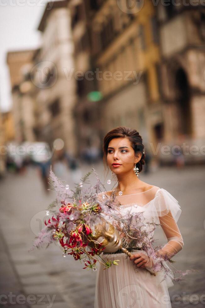 de flicka-brud är med skön blomma mönster som en mask i Florens, eleganta brud i en bröllop klänning stående med en mask i de gammal stad av florens. modell flicka i florens foto