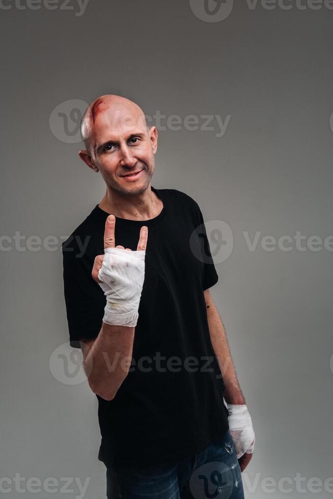 på en grå bakgrund står en misshandlade man i en svart t-shirt med hans händer insvept upp foto