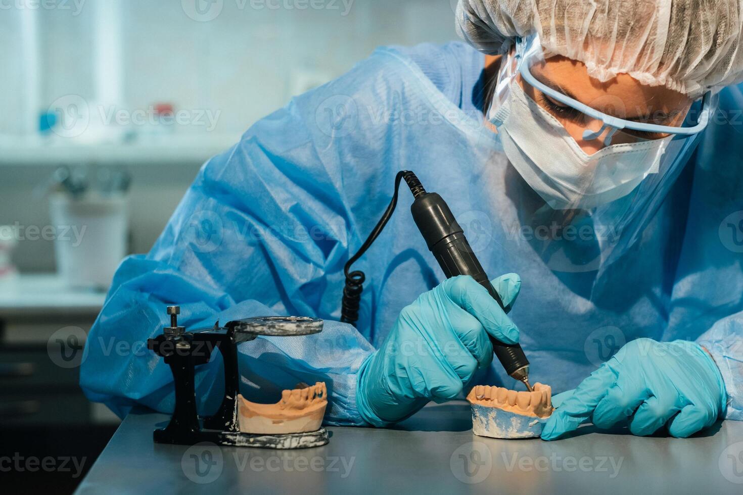 en maskerad och handskar dental tekniker Arbetar på en protes- tand i hans labb foto