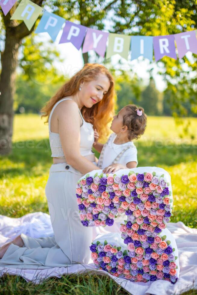 glad mor och dotter har roligt på barn födelsedag på filt med papper dekorationer i de parkera foto